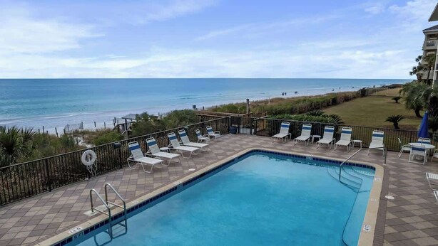 A pool with lounge chairs and a view of the beach. - Huntington By the Sea 501 (Miramar Bch)