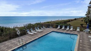 A pool with lounge chairs and a view of the beach.