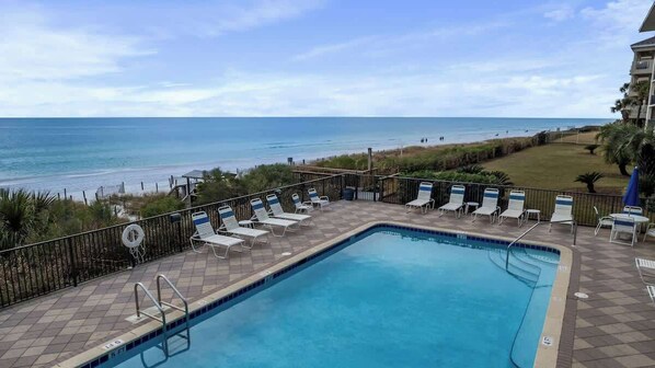 A pool with lounge chairs and a view of the beach.