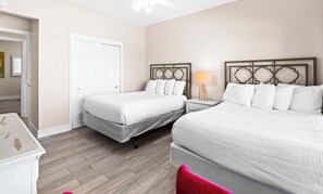 A hotel room with two beds, a nightstand, a lamp, and a door.