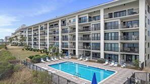A multi-story hotel with balconies, a swimming pool, and outdoor seating.
