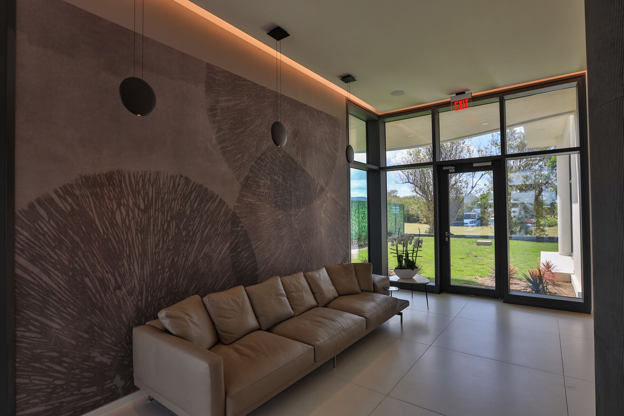 Een modern interieur met een beige bank, een groot abstract wanddecor en grote ramen met uitzicht op het buiten.