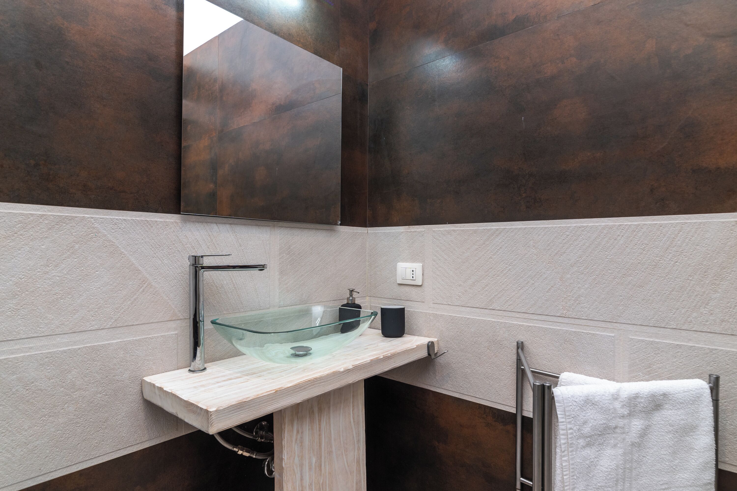 A modern bathroom with a glass sink, a towel rack, and a mirror.