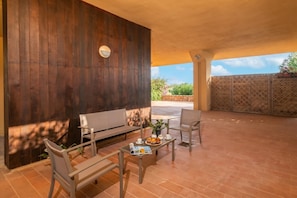 An outdoor patio with a wooden wall, seating, a table with a magazine, and a view of greenery. - Secret Garden House (Olbia)