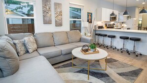 Ein modernes Wohnzimmer mit grauem Sofa, einem Couchtisch und einer Küchenzeile mit Bar und Hockern.