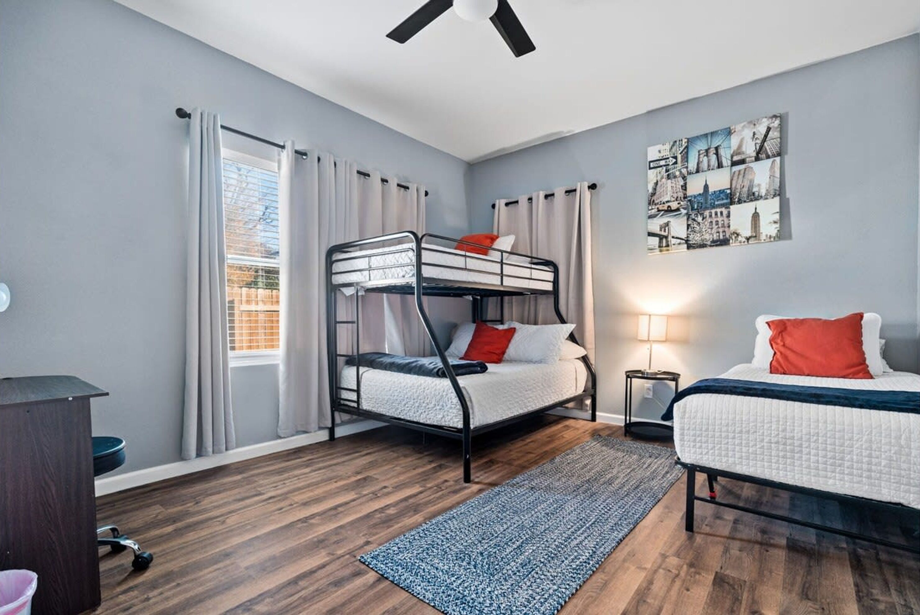 Habitación tipo dormitorio con literas, un escritorio, una lámpara de pie y una obra de arte con vistas a la ciudad en la pared.