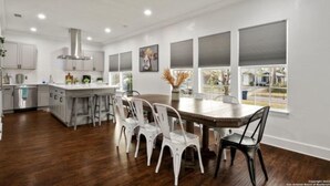 A modern kitchen with white cabinets, a stainless steel range hood, and a dining area with white chairs and a wooden table. - Experience Serenity in a 4BR 3BA Downtown Home (San Antonio)