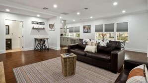 A spacious living room with a dark brown leather sofa, a wooden coffee table, and a striped rug. There is a kitchen area with white cabinets and a dining table. - Experience Serenity in a 4BR 3BA Downtown Home (San Antonio)