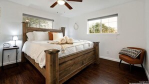 A bedroom with a wooden bed, a ceiling fan, a nightstand, a chair, and two windows. - Experience Serenity in a 4BR 3BA Downtown Home (San Antonio)