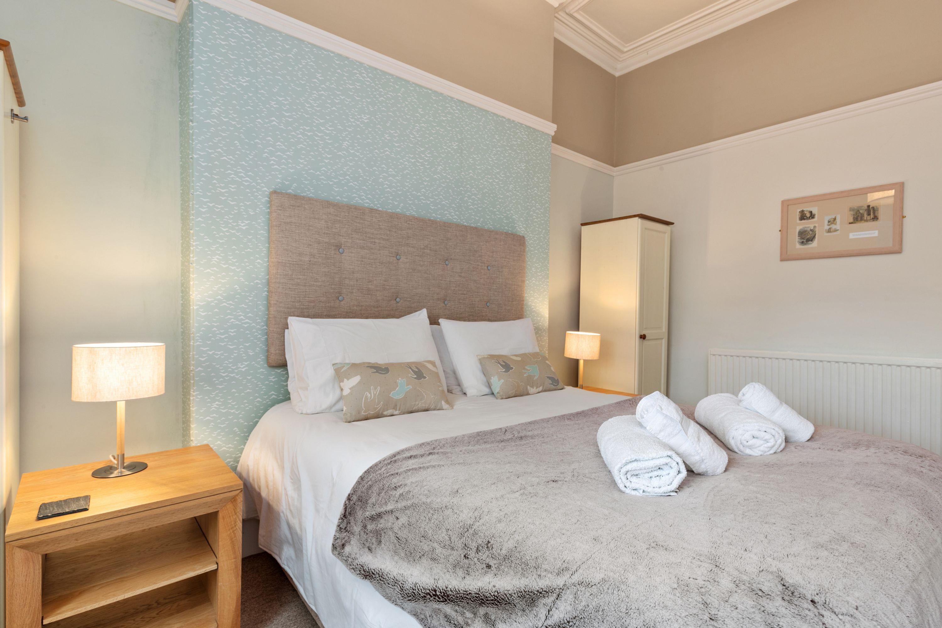 A neatly made bed with a fluffy blanket, two bedside lamps, and a small wooden nightstand with a lamp and a remote control.