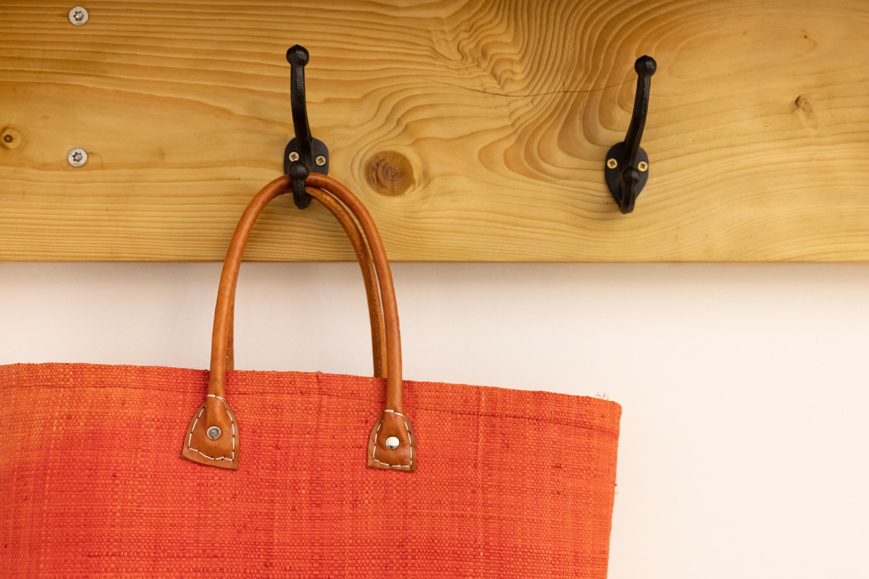 A wooden wall with two black hooks and a red fabric bag hanging from them.