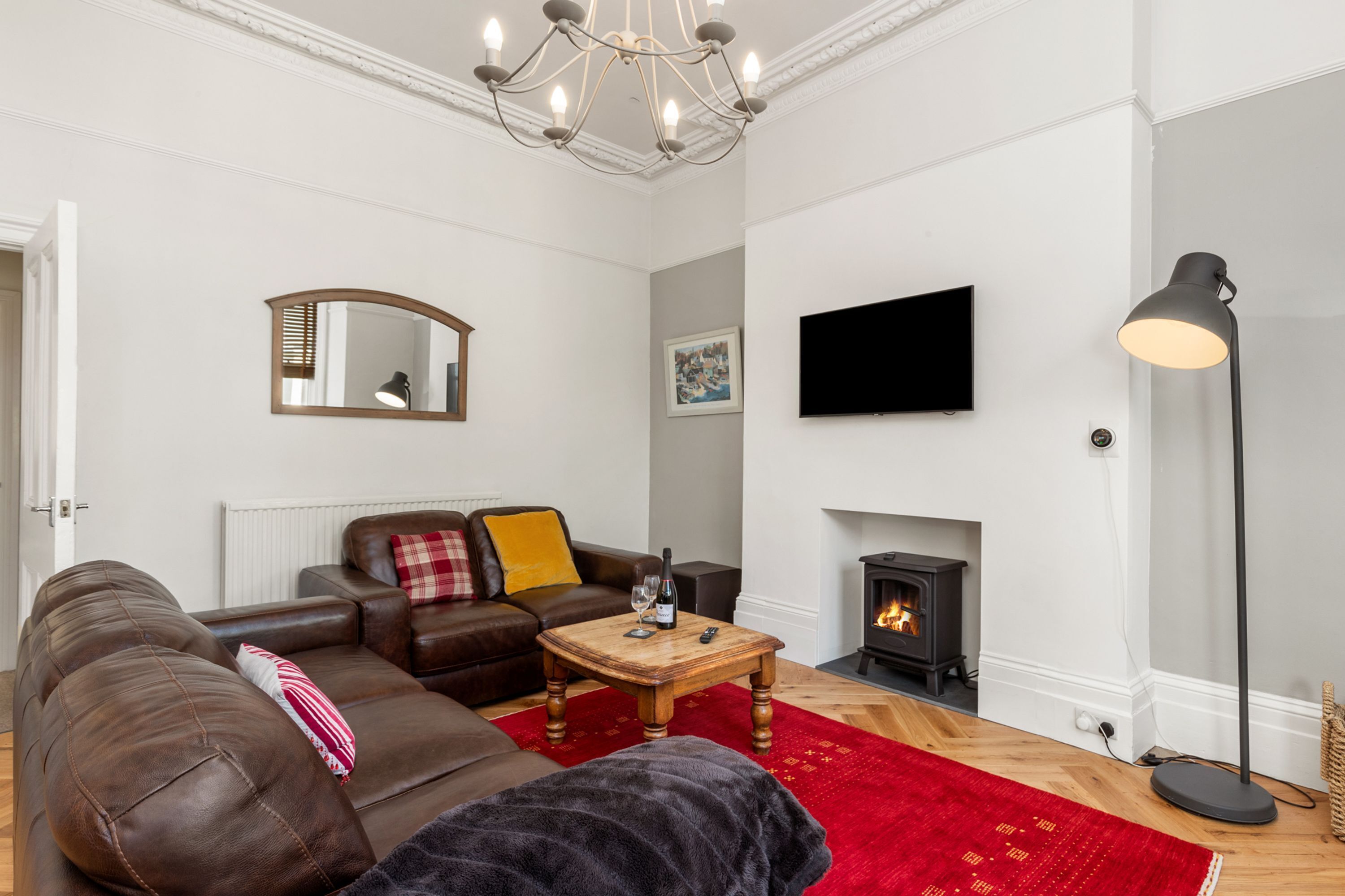 A living room with a brown leather sofa, a wooden coffee table, a red rug, a fireplace, a television, and a floor lamp.