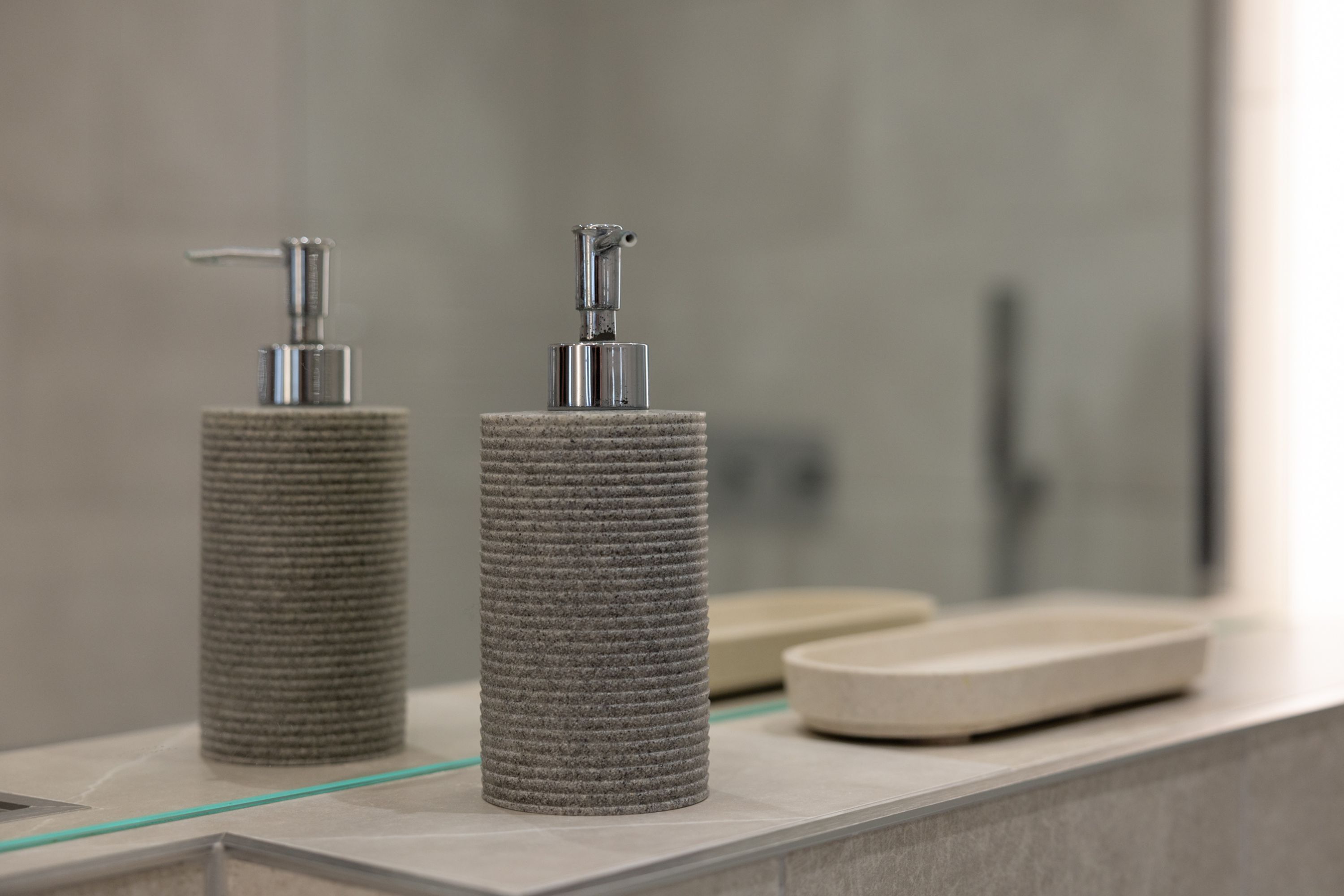 Two cylindrical dispensers on a bathroom counter with a mirror in the background.