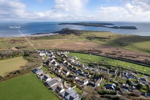 An aerial view of a coastal village with houses, green fields, and the sea in the background. - The Cwtch Apartment - Sea Views Walk to Beach (Tenby)