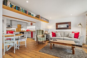 A modern living room with a sofa, coffee table, and a dining area with chairs and a table. There is a kitchen in the background with a microwave and cabinets. - The Cwtch Apartment - Sea Views Walk to Beach (Tenby)