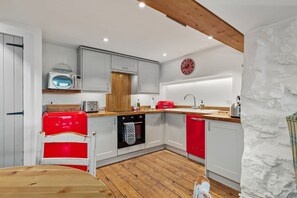 A kitchen with white cabinets, a red refrigerator, a wooden ceiling, and a stone wall. - The Cwtch Apartment - Sea Views Walk to Beach (Tenby)
