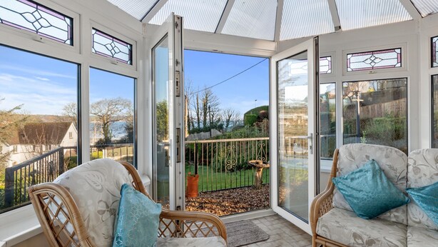 A conservatory with wicker furniture and a view of a garden. - Four Oaks - Sea and Harbour Views (Saundersfoot)
