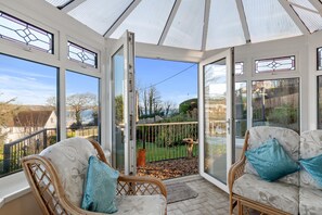 A conservatory with wicker furniture and a view of a garden. - Four Oaks - Sea and Harbour Views (Saundersfoot)