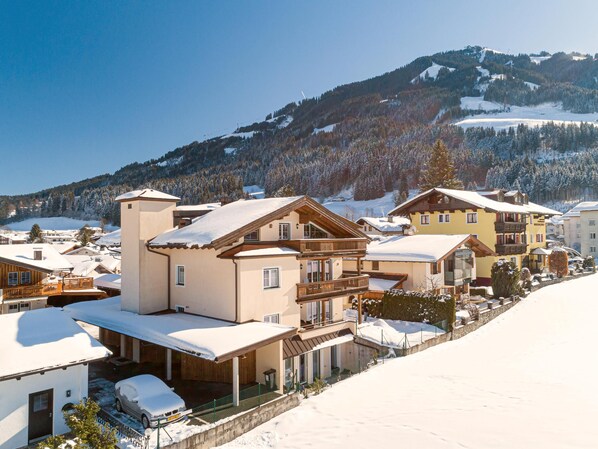 A snow-covered mountain resort with chalet-style buildings, a ski slope in the background, and a clear blue sky.