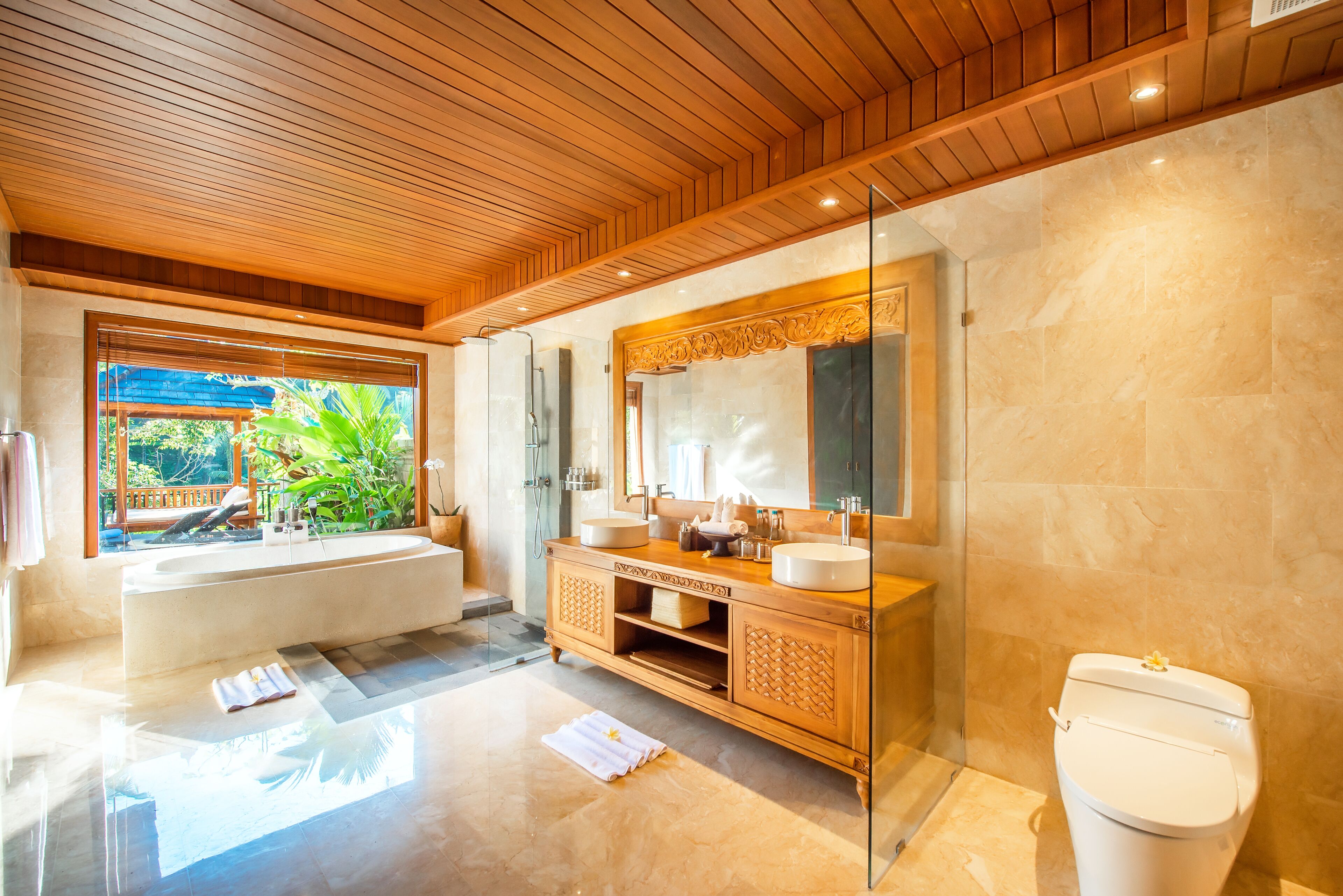 Un baño moderno con techo de madera, un espejo grande, dos lavamanos, una bañera y un inodoro.