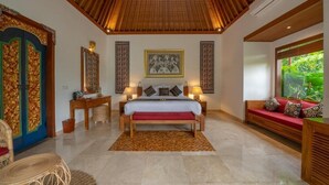 Un dormitorio amplio con techo de madera, una cama grande con colchón rojo, dos mesitas de noche con lámparas, un banco de madera y un ventanal con vistas al verdor.