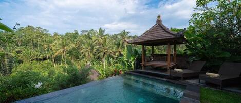 A serene infinity pool with a wooden gazebo and lounge chairs, surrounded by lush tropical vegetation.