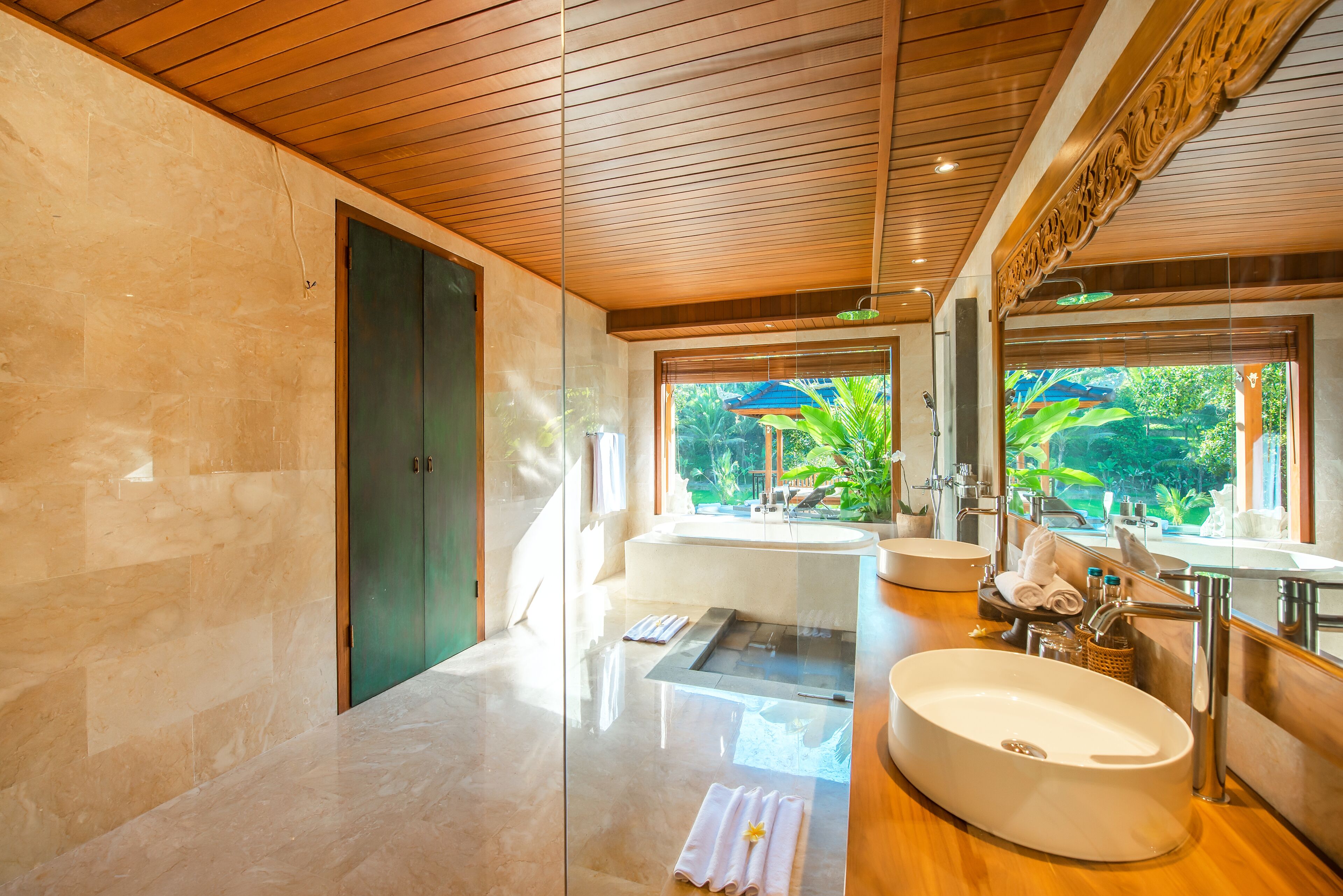 A modern bathroom with a large sink, a mirror, and a window with a view of greenery.