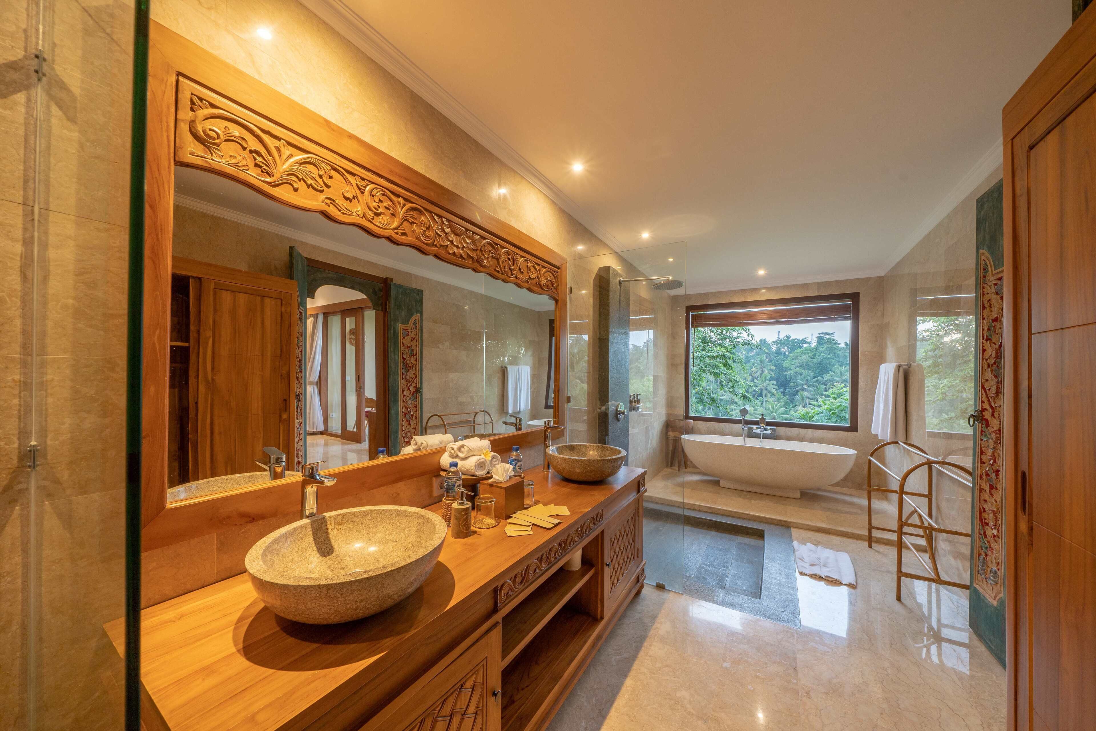 A modern bathroom with a large mirror, a bowl sink, a freestanding bathtub, and a view of greenery outside.