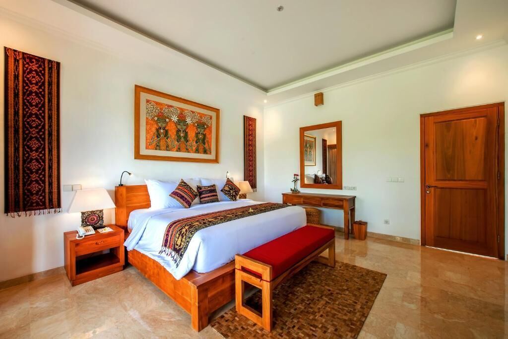 A well-lit bedroom with a large bed, bedside tables, a bench, a desk, and a mirror.