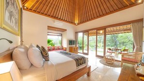 Un dormitorio con techo de madera, una cama con almohadas, un televisor y vistas al exterior.