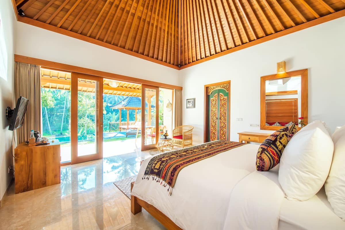 A spacious bedroom with a large bed, wooden ceiling, sliding glass doors leading to a patio, and a wooden nightstand.