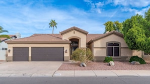 A two-story house with a beige facade, two garage doors, a small front yard with landscaping, and a clear blue sky. - NEW! Luxury, Scottsdale Getaway! (Scottsdale)