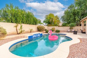 A swimming pool with a pink flamingo float, surrounded by a landscaped garden with various plants and a brick wall. - NEW! Luxury, Scottsdale Getaway! (Scottsdale)