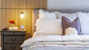 A neatly made bed with white linens and a decorative pillow, a bedside table with a lamp, and a wall with vertical slats. - NEW! Luxury, Scottsdale Getaway! (Scottsdale)