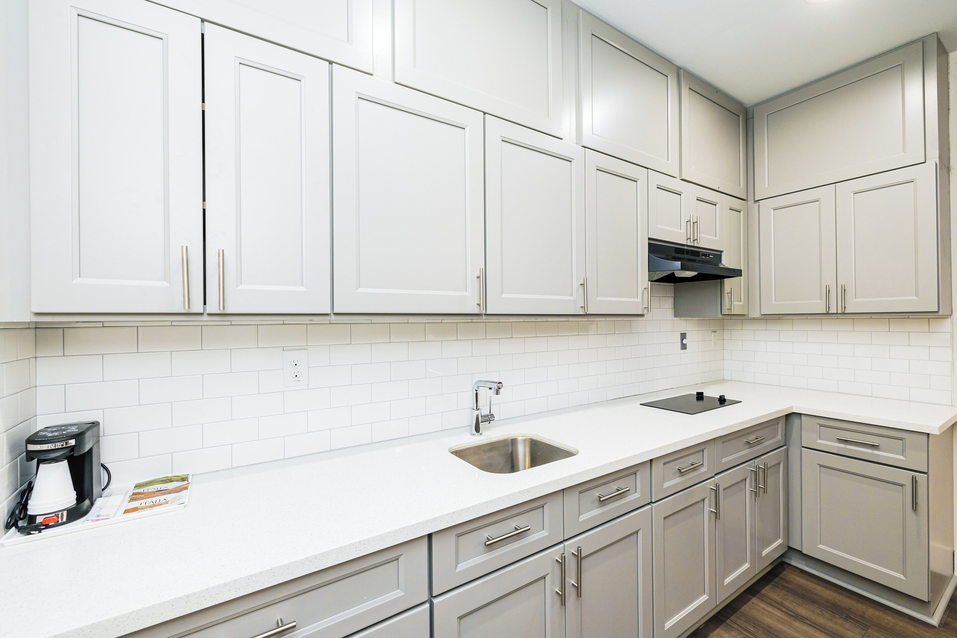 A modern kitchen with white cabinets, a stainless steel sink, and a coffee maker.