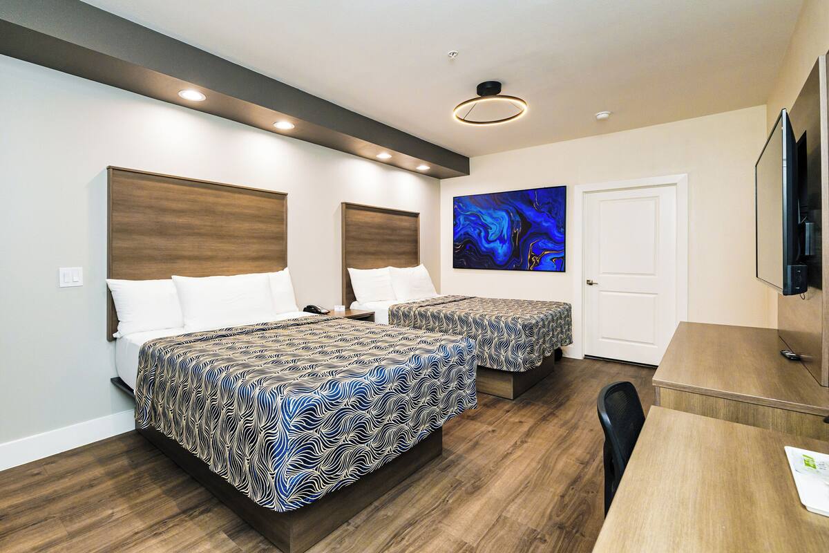A modern bedroom with two beds, a desk, and a TV.