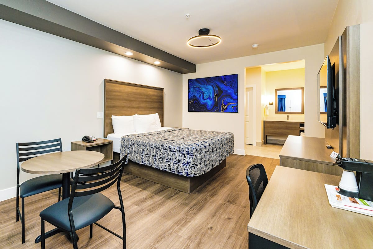 A modern hotel room with a bed, a desk, a chair, a table, and a TV.