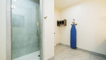 A bathroom with a glass-enclosed shower, a blue towel hanging on a rack, and a small shelf with an iron.