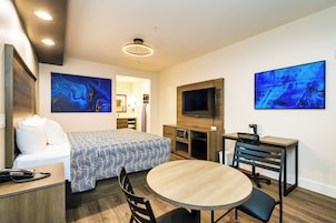 Une chambre d’hôtel moderne équipée d’un lit, d’un bureau, d’une table ronde et de deux grandes peintures abstraites.