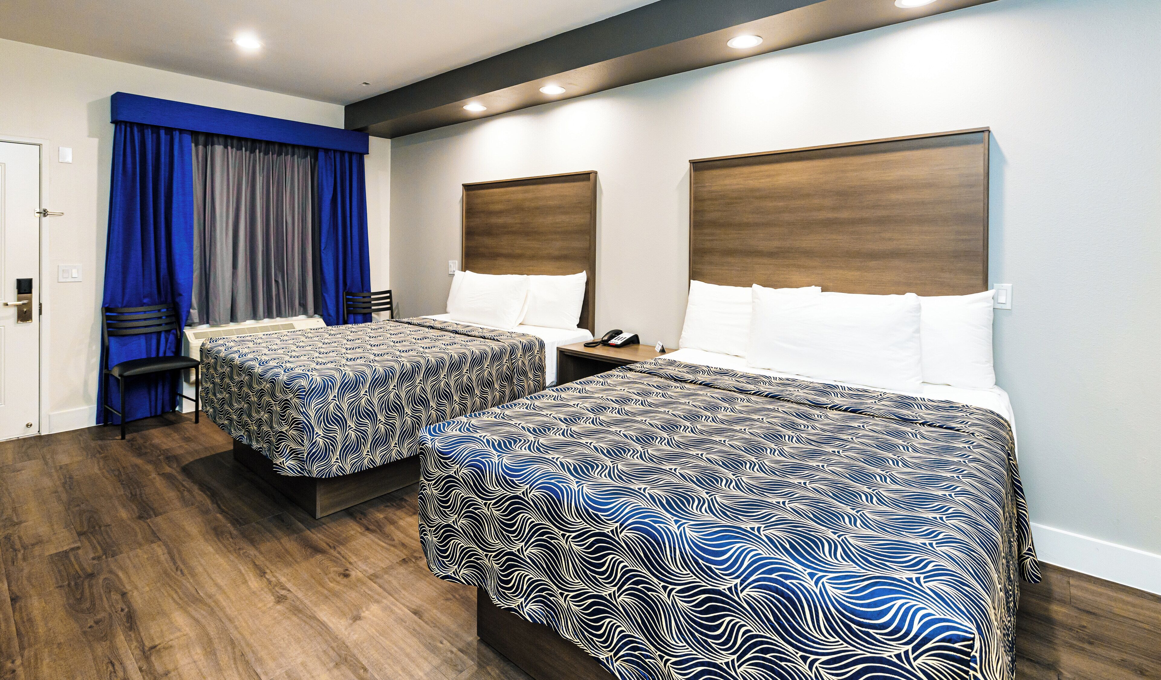 A hotel room with two beds, a blue chair, a desk, and a phone on the nightstand.
