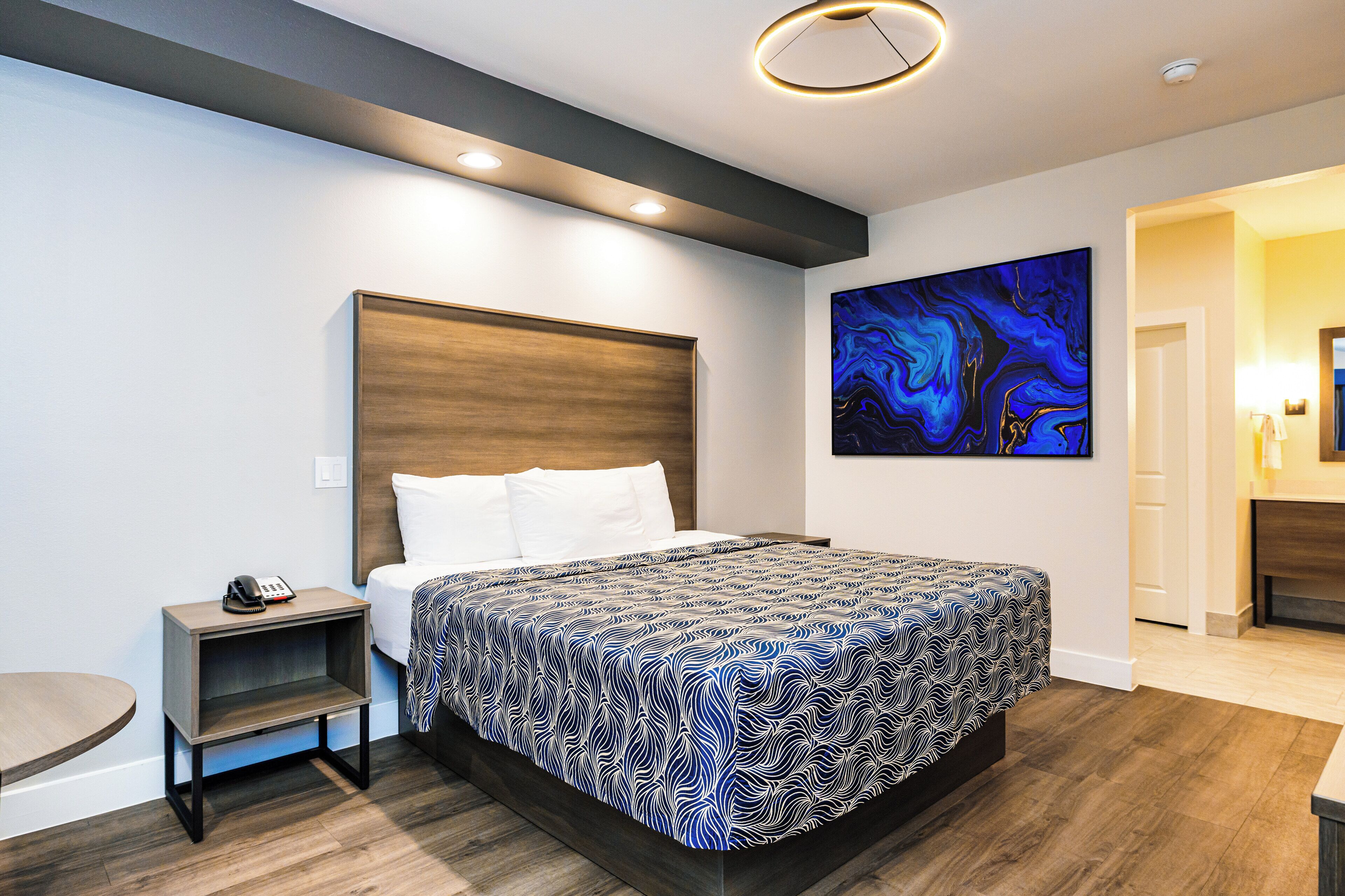 Ein modernes Hotelzimmer mit einem großen Bett, einem Nachttisch mit Telefon, einer kleinen Ablage und einem Bild an der Wand.
