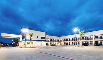A modern hotel with a central courtyard, multiple balconies, and a parking area.