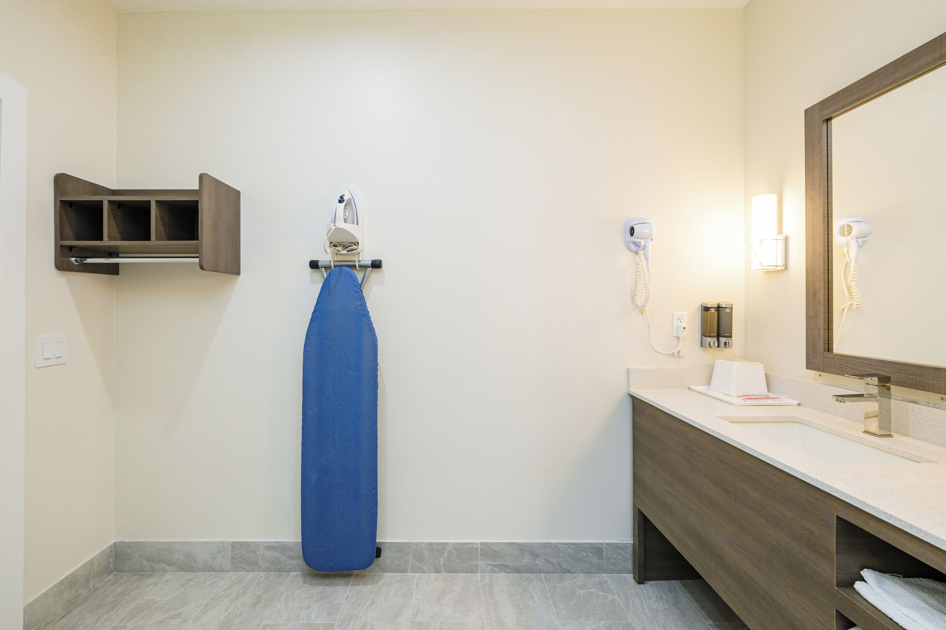 Un baño con cortina de ducha azul, tocador de madera, espejo y secador de pelo en la pared.