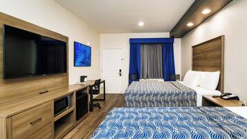 A hotel room with two beds, a desk, a TV, and a door.