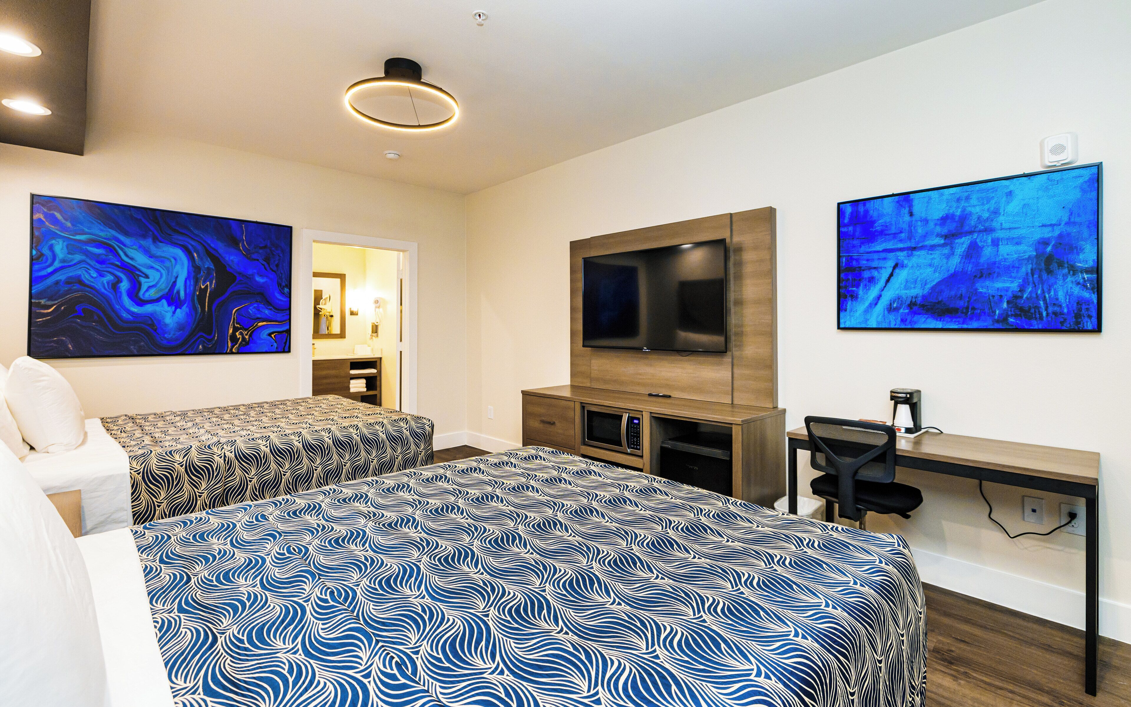 Una habitación de hotel moderna con dos camas, un escritorio, un televisor y obras de arte en las paredes.
