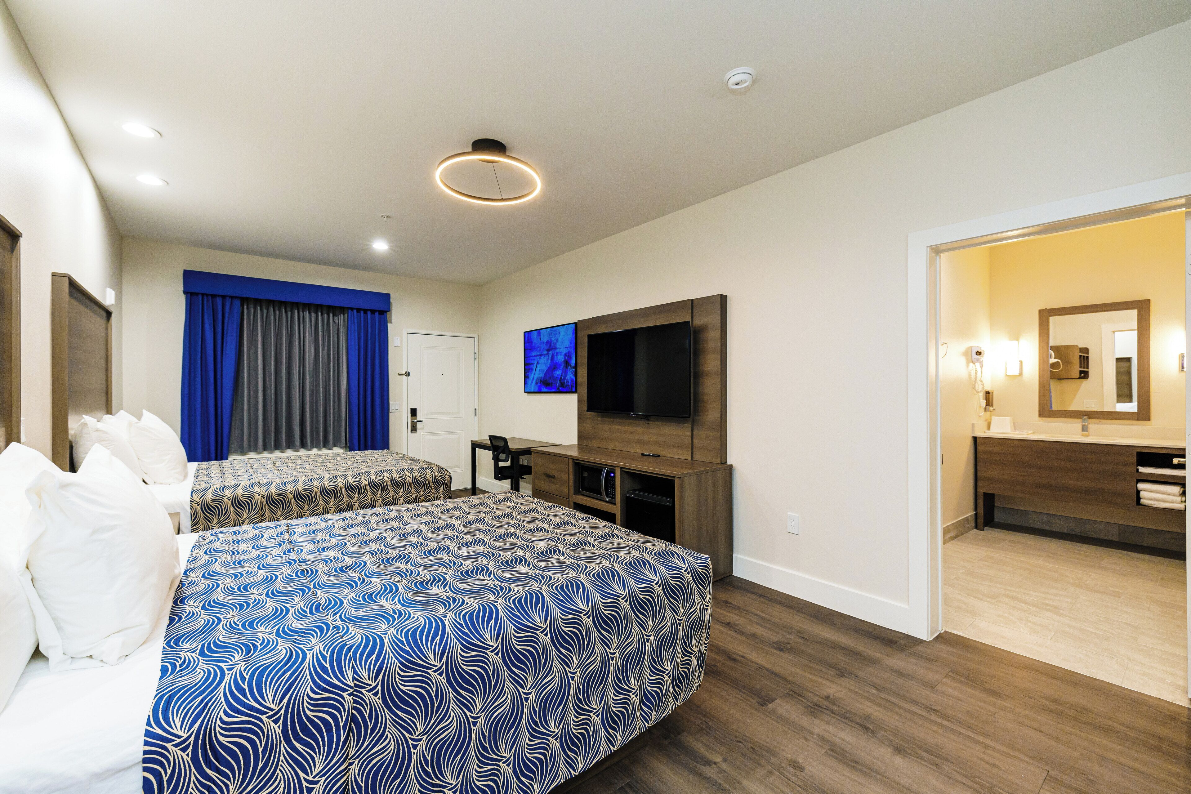 A hotel room with two beds, a TV, a desk, and a bathroom visible through an open door.