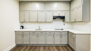 A modern kitchen with light gray cabinets, a white countertop, and a dark wood floor. -  Palace Inn Blue Edgebrook (Houston)