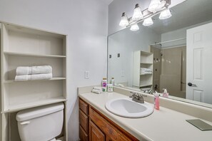 Une salle de bain avec un lavabo blanc, un miroir et des étagères où sont rangées des serviettes.
