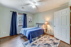 Une chambre à coucher avec un lit, une table de chevet, une lampe, un ventilateur de plafond et une porte.