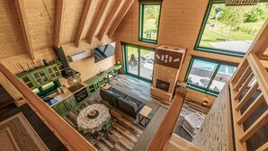 A spacious loft-style room with a high ceiling, a dining area with a round table and chairs, a sofa, and a fireplace.